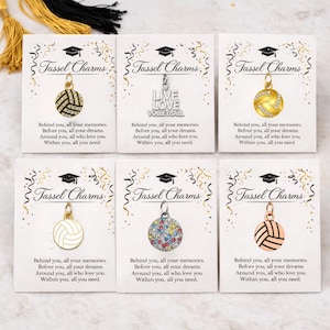 May include: Six volleyball-themed tassel charms on cards. Each charm is a volleyball design, some with crystal accents. One card reads "LIVE LOVE VOLLEYBALL". The cards have graduation cap graphics and the text "Tassel Charms".