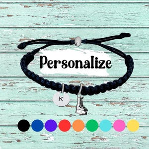 May include: Black braided bracelet with a silver roller skate charm and a round charm with the letter "K". The word "Personalize" is written across the center. Colour options are shown below.