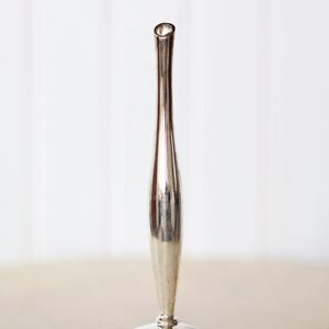 May include: A tall, slender silver vase with a flared base and a narrow opening. The vase has a smooth, reflective surface and stands approximately 10 inches tall. The design is minimalist and elegant, suitable for a single stem or as a decorative object.