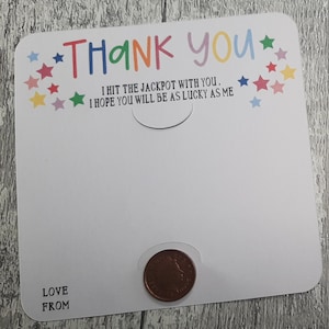 May include: A white card with rounded corners, featuring the words "THANK YOU" in colorful letters and star accents. The text "I HIT THE JACKPOT WITH YOU. I HOPE YOU WILL BE AS LUCKY AS ME" is also printed on the card. A penny is placed in a circular cutout.