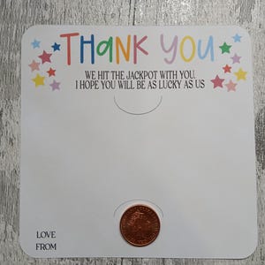 May include: A white card with the words "THANK YOU" in colorful letters and the text "WE HIT THE JACKPOT WITH YOU. I HOPE YOU WILL BE AS LUCKY AS US." A penny is placed in a circular cutout. The words "LOVE FROM" are at the bottom.