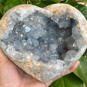May include: A heart-shaped geode with a light blue crystal interior. The geode is made of a rough, brown stone.