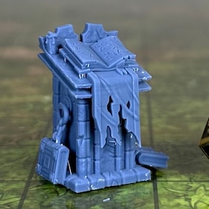 May include: A blue plastic miniature of a stone altar with a book on top and a tattered banner hanging from the side. A gold and black 20-sided die is next to the altar.