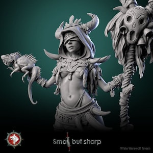 Puede incluir: Una figura gris y detallada de una mujer con una venda en los ojos, cuernos y plumas. Ella sostiene un lagarto en una mano y un bastón con una máscara tallada en la otra. La figura está hecha de un material liso y mate.