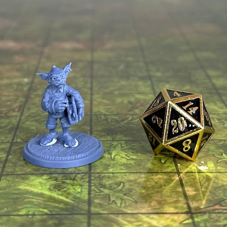 May include: A gray plastic miniature figurine of a goblin playing a musical instrument. The goblin is wearing a hat and holding a drum. The figurine is standing on a gray base. A black and gold 20-sided die is in the background.