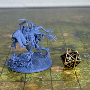 May include: A blue-grey miniature creature figure with multiple spindly limbs and a hooded head, standing on a circular base next to a black and gold twenty-sided die with gold numbers, showing the number 20 on the top-facing triangular facet.