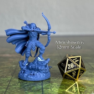Könnte beinhalten: Eine blaue Plastik-Miniaturfigur eines Kapuzenbogenschützen mit Bogen und Pfeil, stehend auf einem felsigen Sockel. Die Miniatur ist im Maßstab 32 mm, wie der Text "Mini shown is 32mm Scale" angibt. Neben der Miniatur ist ein schwarzer und goldener 20-seitiger Würfel zu sehen.