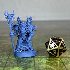 Puede incluir: Una miniatura de pl&aacute;stico azul de un personaje de fantas&iacute;a que sostiene un bast&oacute;n con calaveras. El personaje lleva armadura y tiene barba. La miniatura est&aacute; de pie sobre una base redonda. Un dado de 20 caras negro y dorado est&aacute; en el fondo.