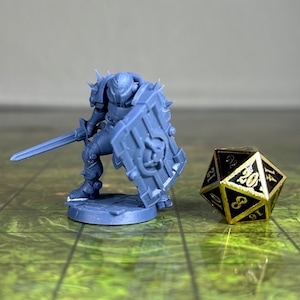 May include: A gray plastic miniature figure of a warrior wearing armor and holding a sword and shield. The figure is standing on a round base. A gold metal 20-sided die is in the background.