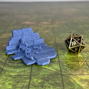 Puede incluir: Una miniatura de plástico azul de un esqueleto tumbado sobre un muro de piedra roto, con un dado de 20 caras en el fondo.