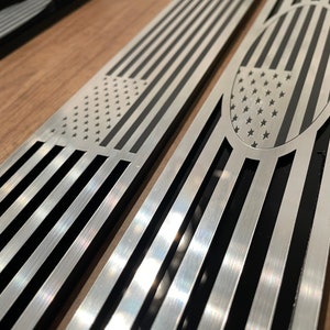 May include: Two stainless steel car door sill plates with an American flag design. The plates have a black background with a silver outline and a silver American flag design.