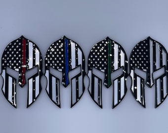 May include: Four black Spartan helmet decals with an American flag design. Each helmet has a thin coloured stripe representing a different first responder group: red for firefighters, blue for police, green for EMT, and black for military.