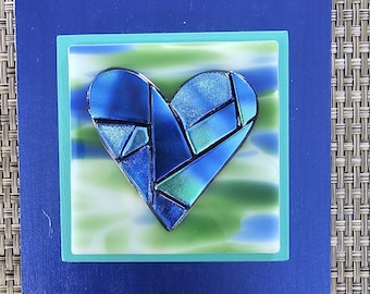 Corazón de cristal azul verdoso con corazón de cristal dicroico fusionado sobre cristal azul y verde y marco azul, obra de arte mural de Gary Levin.