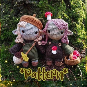 Peut inclure: Deux poupées elfes en crochet avec des chapeaux en forme de champignon et des tenues brunes. L'elfe de gauche tient un gland brun et l'elfe de droite tient un panier de champignons. Les poupées sont assises sur un lit de mousse avec un fond vert.
