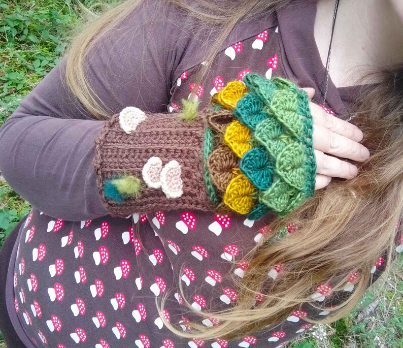 Puede incluir: Guantes de mu&ntilde;eca de ganchillo hechos a mano en marr&oacute;n, verde y amarillo. Los guantes de mu&ntilde;eca presentan un dise&ntilde;o de tronco de &aacute;rbol con acentos de seta y un patr&oacute;n de hojas. Ideales para oto&ntilde;o o invierno.