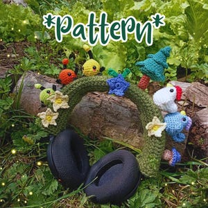 Op de afbeelding: Een zwarte koptelefoon rust op een boomstam, versierd met een gehaakte groene krans. De krans is versierd met kleurrijke gehaakte bloemen, insecten en andere grillige elementen. Het woord "Pattern" is in groene letters geschreven.