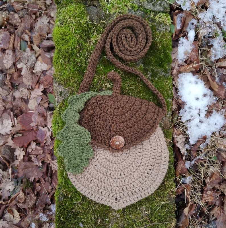 May include: A brown and beige crocheted acorn-shaped purse with a green crocheted leaf and a brown button. The purse has a brown crocheted strap.
