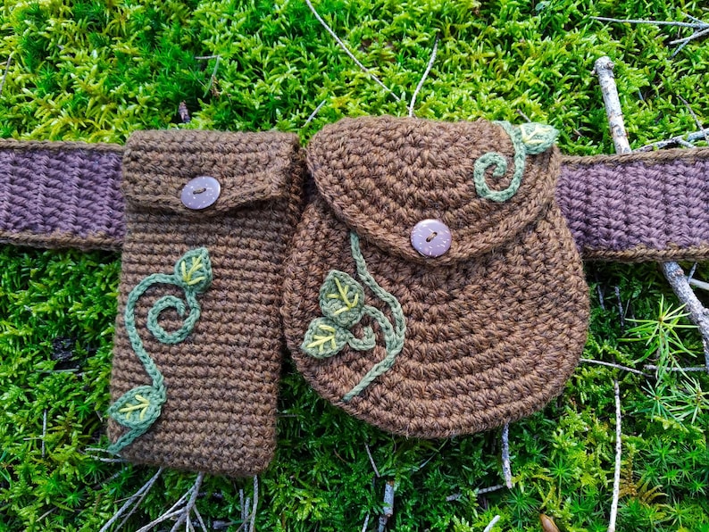 K&ouml;nnte beinhalten: Ein brauner geh&auml;kelter G&uuml;rtel mit zwei Taschen und einem Blatt-Ranken-Design. Die Taschen haben einen Knopfverschluss und sind perfekt f&uuml;r die Aufbewahrung von Kleinigkeiten.