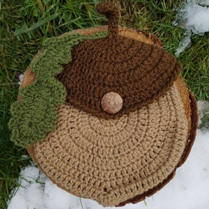 May include: A crocheted acorn hat with a brown cap, a tan bottom, and a green leaf. The hat has a wooden button.