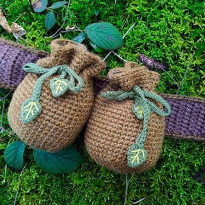 K&ouml;nnte beinhalten: Zwei braune H&auml;kelbeutel mit gr&uuml;nen Blattembroidery und braunen B&auml;ndern. Die Beutel liegen auf einem Bett aus gr&uuml;nem Moos.