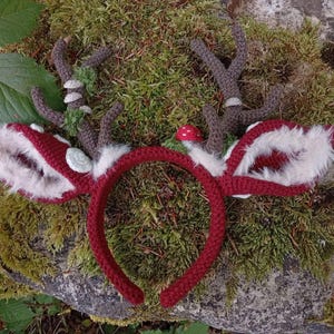 May include: A handmade red crochet headband with deer antlers and ears. The antlers are brown with green accents, and the ears are red with white faux fur trim. A small red mushroom is attached to the headband.