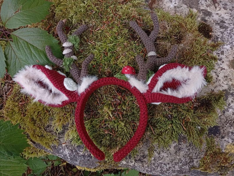 May include: A handmade red crochet headband with deer antlers and ears. The antlers are brown with green accents, and the ears are red with white faux fur trim. A small red mushroom is attached to the headband.