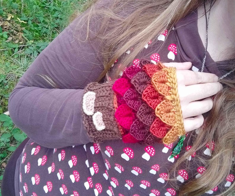 Puede incluir: Calentadores de brazo de ganchillo en tonos marr&oacute;n, rojo y naranja. Los calentadores de brazo presentan un dise&ntilde;o de escamas, con un pu&ntilde;o marr&oacute;n adornado con acentos blancos en forma de hongo. La manga es visible en color marr&oacute;n oscuro.