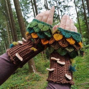 Puede incluir: Guantes sin dedos de ganchillo con tem&aacute;tica de bosque. Los pu&ntilde;os son marrones, parecidos a la corteza de un &aacute;rbol, con detalles de setas blancas. La parte superior presenta escamas verdes, amarillas y marrones con forma de hoja. El fondo es un bosque.