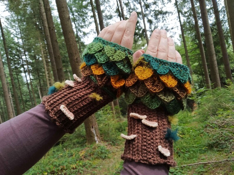 Puede incluir: Guantes sin dedos de ganchillo con tem&aacute;tica de bosque. Los pu&ntilde;os son marrones, parecidos a la corteza de un &aacute;rbol, con detalles de setas blancas. La parte superior presenta escamas verdes, amarillas y marrones con forma de hoja. El fondo es un bosque.
