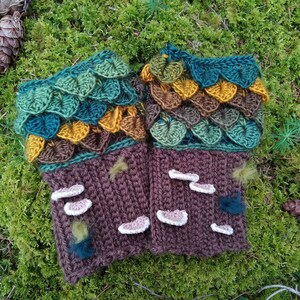 Puede incluir: Un par de guantes sin dedos hechos a mano con ganchillo. Los guantes presentan una base marr&oacute;n con detalles de setas blancas y una secci&oacute;n superior con detalles en forma de hojas verdes, turquesas, marrones y amarillas. Sobre un fondo de musgo.