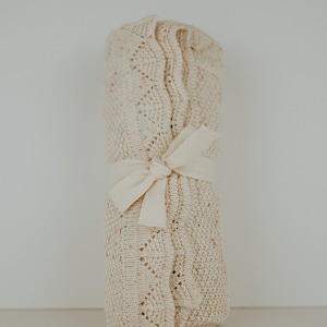 May include: A cream-colored knitted baby blanket with a delicate pattern, rolled up and tied with a white ribbon.