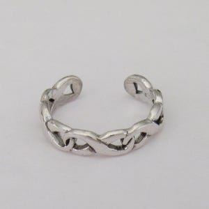 May include: A silver-colored toe ring with a chain link design. The ring is open at the top, allowing for adjustment. The links are interlocked, creating a continuous pattern. The ring is set against a plain white background.
