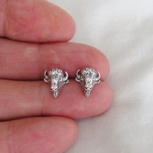 May include: A pair of silver buffalo head stud earrings. The earrings are small and detailed, with a realistic depiction of a buffalo's head.