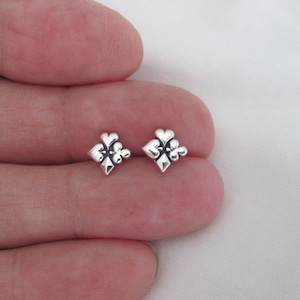 May include: A pair of silver stud earrings featuring a design of four overlapping hearts, resembling a playing card suit.