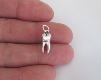 May include: A silver charm in the shape of a tooth. The charm is about the size of a fingernail and has a loop at the top for attaching to a chain or bracelet.