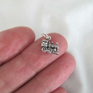 May include: A silver charm in the shape of a small train engine. The charm is detailed with a black painted finish and is perfect for adding a touch of whimsy to a bracelet or necklace.
