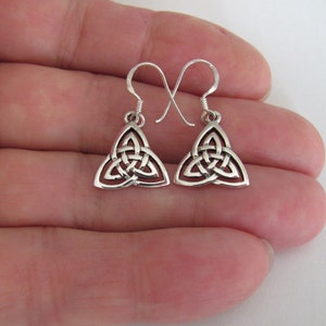 May include: A pair of silver-colored Celtic Trinity knot dangle earrings. Each earring features a triangular design with an interwoven knot pattern and a curved hook for pierced ears. The earrings are displayed against a light background.