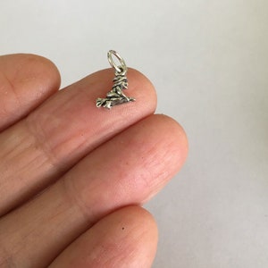 May include: A small silver charm of a witch riding a broomstick.