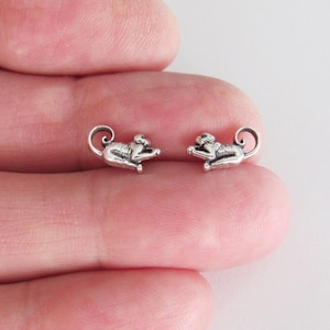 May include: A pair of silver monkey stud earrings. The monkeys are facing forward with their tails curled up behind them.