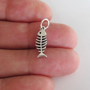 May include: Silver charm in the shape of a fish skeleton. The charm has a loop at the top for attaching to a necklace or bracelet.