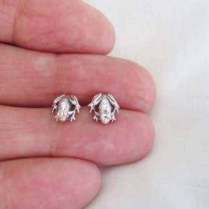 May include: A pair of silver frog stud earrings. The frogs are facing forward with their legs outstretched. The earrings are small and delicate.