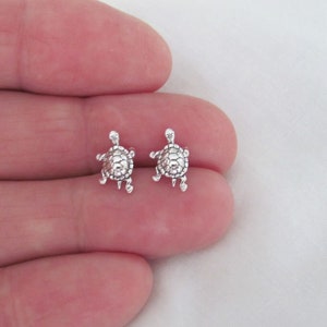 May include: A pair of silver turtle stud earrings. The turtles are facing forward with their heads up and their legs outstretched.