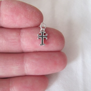 May include: A small silver charm in the shape of a cross with a black enamel finish. The cross has a simple design with a slightly ornate border.