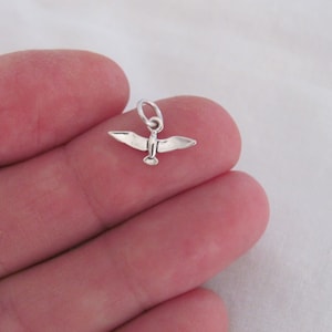 May include: A silver charm in the shape of a bird with its wings spread out.