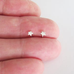 May include: A pair of small, silver-colored star-shaped stud earrings. The earrings are displayed on a light-colored background, showcasing their simple, yet elegant design. These earrings are a subtle accessory.