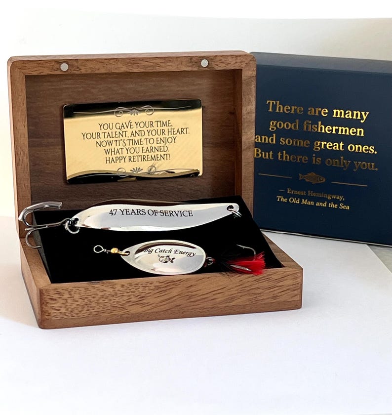 May include: A wooden box containing two silver fishing lures. The top lure is engraved with 47 YEARS OF SERVICE. The bottom lure features the text Big Catch Energy. A gold plaque inside reads YOU GAVE YOUR TIME, YOUR TALENT, AND YOUR HEART.