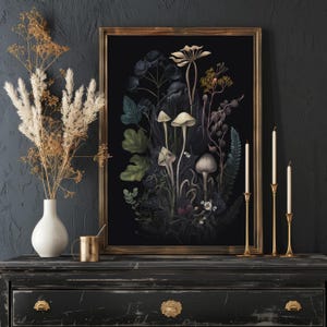 K&ouml;nnte beinhalten: Ein gerahmter botanischer Druck mit dunklem Hintergrund, der Pilze und Pflanzen in Gr&uuml;n, Wei&szlig; und Lila zeigt. Der Druck befindet sich auf einer schwarzen Kommode mit goldenen Kerzenhaltern und einer wei&szlig;en Vase. Der Rahmen ist goldfarben.