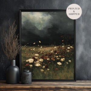May include: A framed art print depicting a field of wildflowers under a dark, stormy sky. The artwork features a palette of dark greens, browns, and creams, with a vintage aesthetic. The print is displayed on a wooden surface.