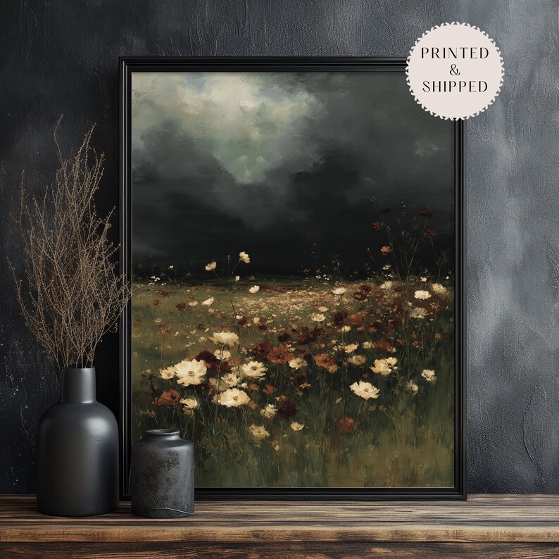 May include: A framed art print depicting a field of wildflowers under a dark, stormy sky. The artwork features a palette of dark greens, browns, and creams, with a vintage aesthetic. The print is displayed on a wooden surface.