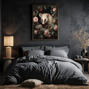 May include: A framed art print featuring a white opossum surrounded by pink roses and greenery. The artwork has a dark, moody aesthetic, with a focus on the opossum's face. The print is displayed above a bed with gray bedding.